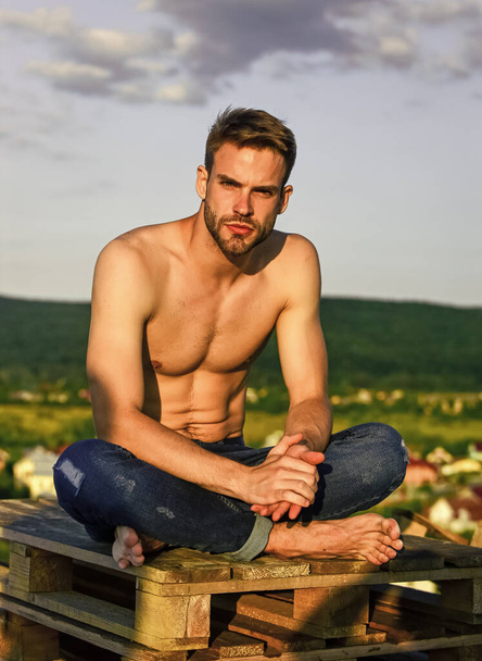 Relaxing after training. sexy man undressed in jeans. male fashion model on sky background. summer relax outdoor. athletic sportsman has sexy body. muscular man at sunset. macho man has naked torso - Fotó, kép