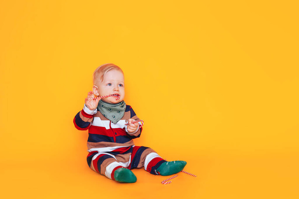 A child in Christmas pajamas sits against a yellow background. Against the background of boxes in green packaging with gifts. Christmas mood. - Fotó, kép