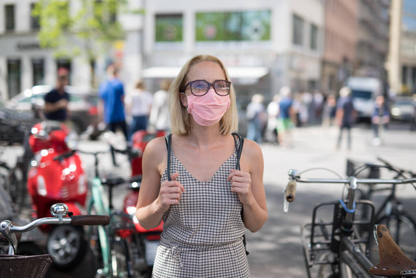 Egy hétköznapi nő arcképe, aki az utcán sétál védőruhában a covid-19 vírus ellen. Véletlenszerű emberek a háttérben - Fotó, kép