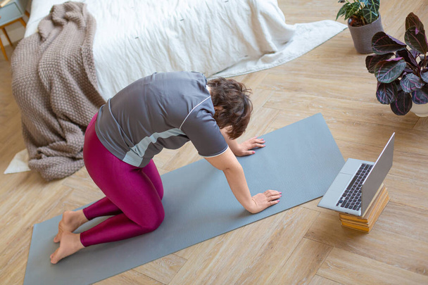 Mulher sênior se exercitando em casa na frente de um monitor de laptop. Alongamento para trás. - Foto, Imagem