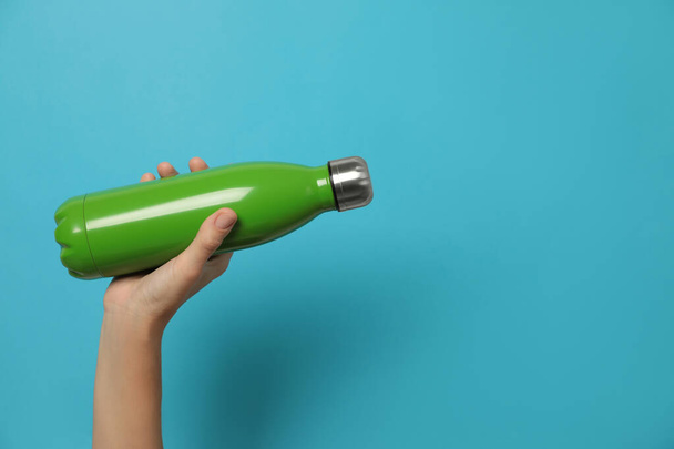 Woman holding modern green thermos on light blue background, closeup. Space for text - Foto, afbeelding