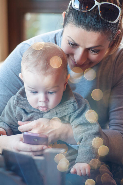 Щаслива мати тримає свого сина на колінах і показує певний вміст на мобільному телефоні. Зимовий сезон
 - Фото, зображення