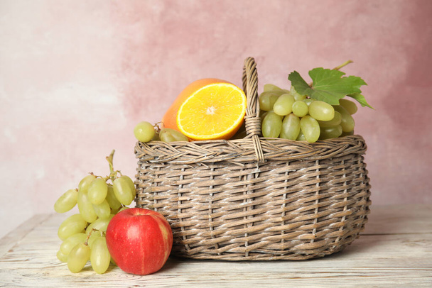Wicker basket with different fruits on white wooden table near pink wall - Photo, Image