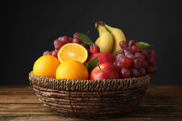 Cesta de mimbre con diferentes frutas en la mesa de madera, primer plano - Foto, Imagen