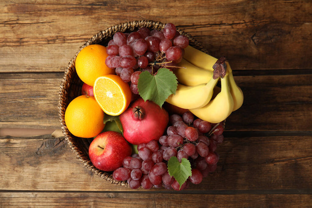 Wicker basket with different fruits on wooden table, top view - Foto, Imagen