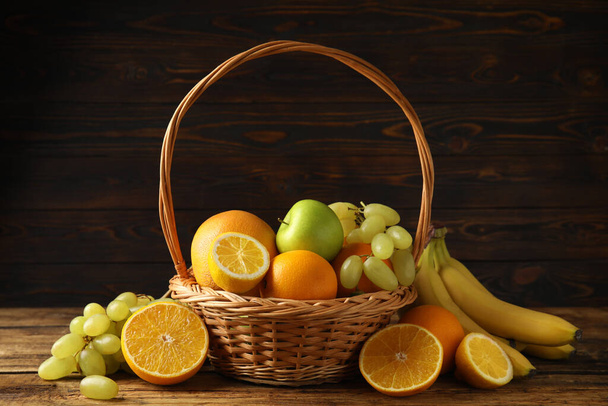 Wicker basket with different fruits on wooden table - Φωτογραφία, εικόνα