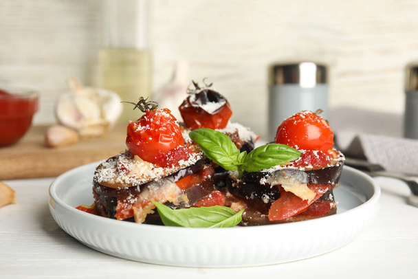 Baked eggplant with tomatoes, cheese and basil served on white wooden table - Foto, Bild