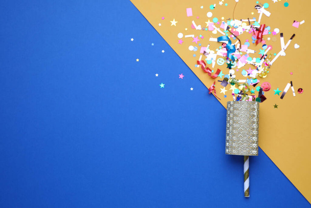 Shiny confetti and party cracker on color background, top view. Space for text - 写真・画像