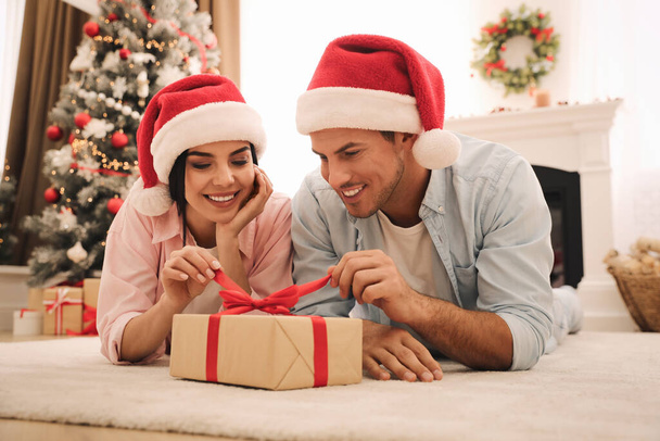Happy couple in Santa hats with Christmas gift at home - Fotoğraf, Görsel