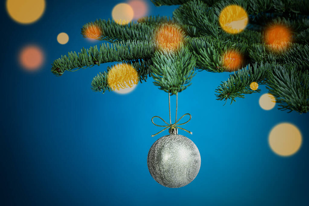 Beautiful Christmas ball hanging on fir tree branch against light blue background, bokeh effect - Foto, afbeelding
