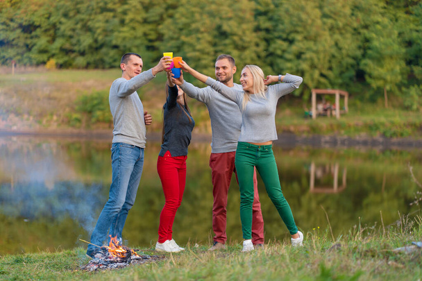 Picnic with friends in at lake near bonfire. Company friends having hike picnic nature background. Hikers relaxing during drink time. Summer picnic. Fun time with friends. - Φωτογραφία, εικόνα