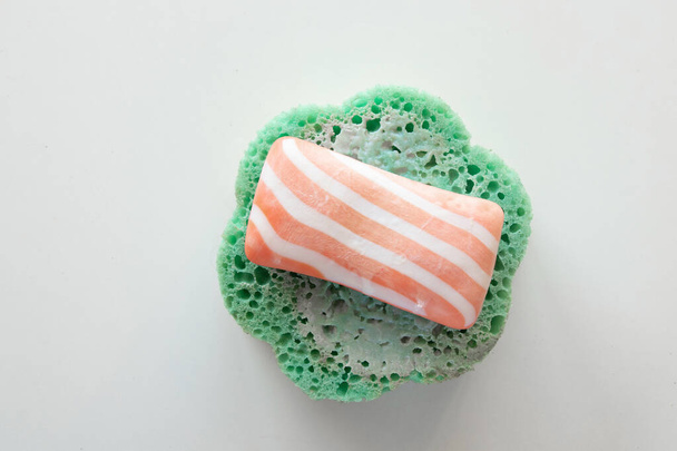 striped soap lies on a wet green sponge on a white background in a bathroom, hygiene products - Photo, Image