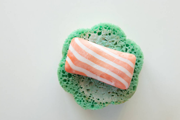 striped soap lies on a wet green sponge on a white background in a bathroom, hygiene products - Φωτογραφία, εικόνα