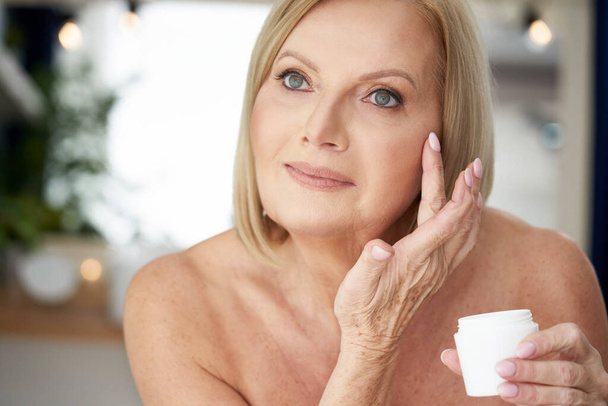 Mujer mayor usando crema anti arrugas en el baño - Foto, imagen