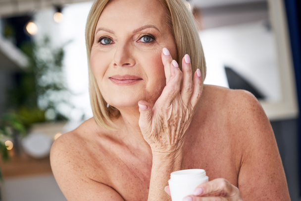 Mujer mayor usando crema anti arrugas en el baño - Foto, imagen