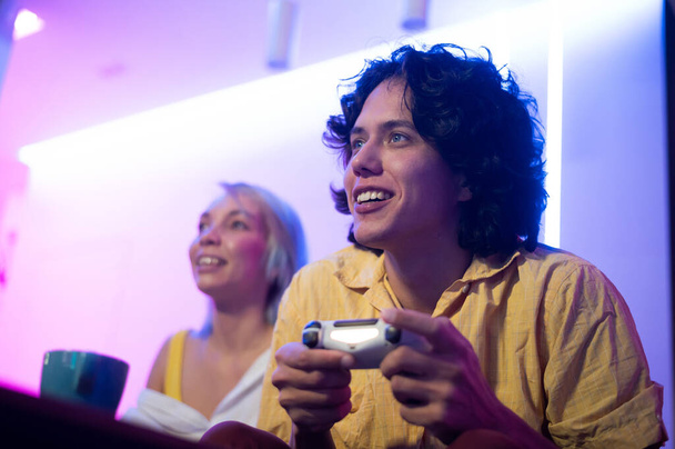Evde video oyunu oynayan gülümseyen bir çift. Gençlerin salgın sırasında birlikte zaman geçirdikleri düşük açılı çekim.. - Fotoğraf, Görsel