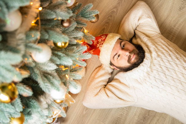 Расслабьтесь Кавказский мужчина среднего возраста лежал под елкой на полу своей собственной квартиры праздничный интерьер помещений пространство отдыха концепция обои плакат реклама - Фото, изображение