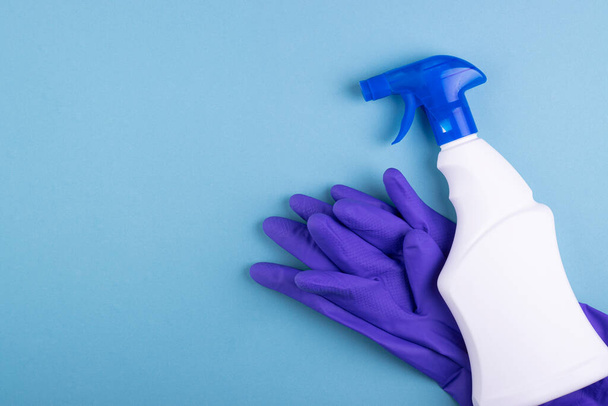 láhev čisticího spreje z bílého skla s gumovými rukavicemi, izolovanou na modrém pozadí. koncepce čistoty a úklidu - Fotografie, Obrázek