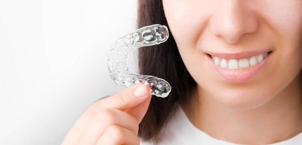 Kapalı bir kadın mükemmel bir gülümseme için şeffaf bir diş teli tutuyor. Diş düzeltme ve beyazlatma için ortodontik hizalayıcılar. - Fotoğraf, Görsel