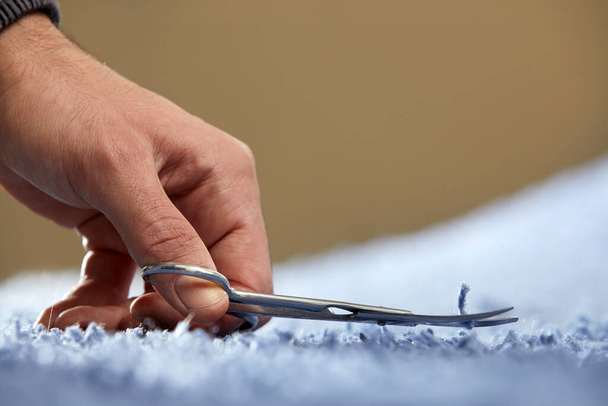 Fechar-se da mão que corta a corda em um carpete com a tesoura. Serviço de limpeza de tapetes - Foto, Imagem
