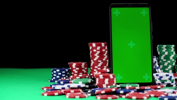 Mobile avec écran vert dans une orientation verticale se tient parmi les piles de jetons de poker en gros plan - Séquence, vidéo