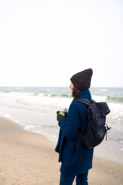 Mooie Kaukasische vrouw wandelen door de zee en het houden van herbruikbare eco-vriendelijke kop koffie - Foto, afbeelding