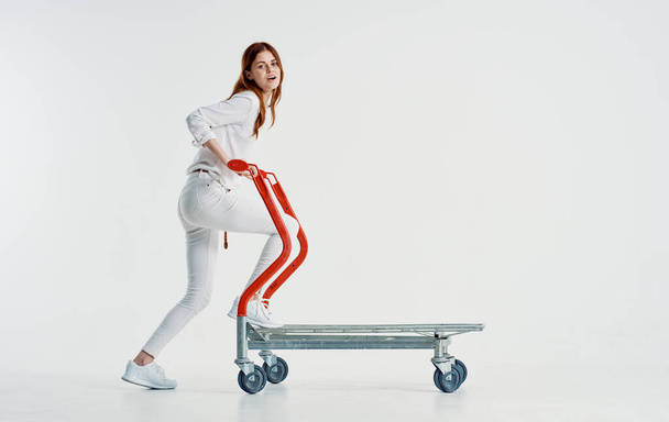 woman courier with a cargo trolley on a light background in full growth - Photo, Image