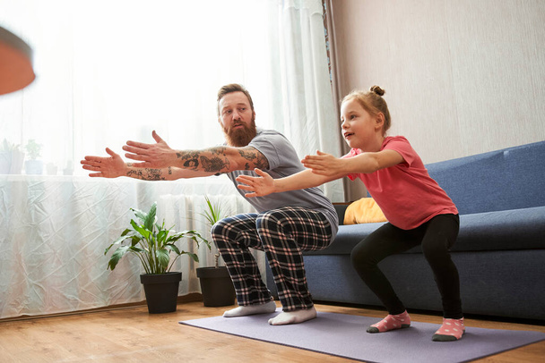 Father and his cute little daughter are doing squat exercises - Foto, Bild