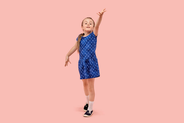 Portrait of a little girl in a beautiful blue polka dot dress. Pink background. - Фото, зображення