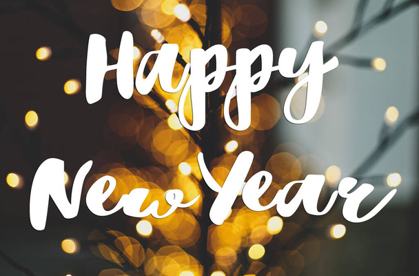 Feliz Año Nuevo tarjeta de felicitación. Feliz Año Nuevo texto escrito a mano en el elegante árbol iluminado con cálidas luces doradas bokeh al aire libre. Saludos de temporada, felices fiestas - Foto, Imagen