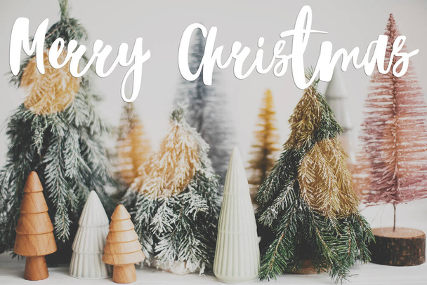 Joyeux Noël carte de voeux. Joyeux Noël texte écrit à la main sur les petits arbres enneigés de Noël dans les lumières sur fond blanc, scène de forêt d'hiver. Joyeuses fêtes, salutations de saison - Photo, image
