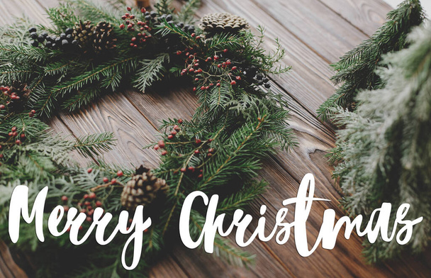 メリークリスマスグリーティングカード。ベリー、松のコーン、自然の木の装飾と現代のクリスマスリースに手書きのメリークリスマステキスト。幸せな休日、季節の挨拶 - 写真・画像