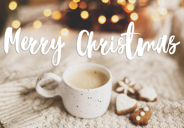 メリークリスマスグリーティングカード。暖かいコーヒーに手書きのメリークリスマステキスト、居心地の良いニットセーター、クリスマスジンジャーブレッドクッキーとライト。幸せな休日、季節の挨拶 - 写真・画像