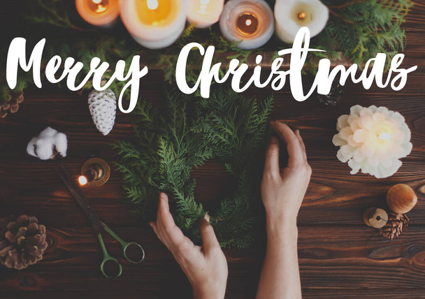 Veselé vánoční přání. Veselý vánoční text ručně psaný na rustikálním vánočním věnci v rukou a svíčkách, borovicové šišky, nůžky na tmavém dřevě, plochý ležel. Veselé svátky, roční pozdravy - Fotografie, Obrázek