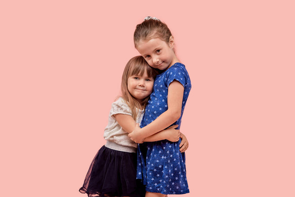 Two cute little girls sisters hug tightly and look at the camera. - 写真・画像