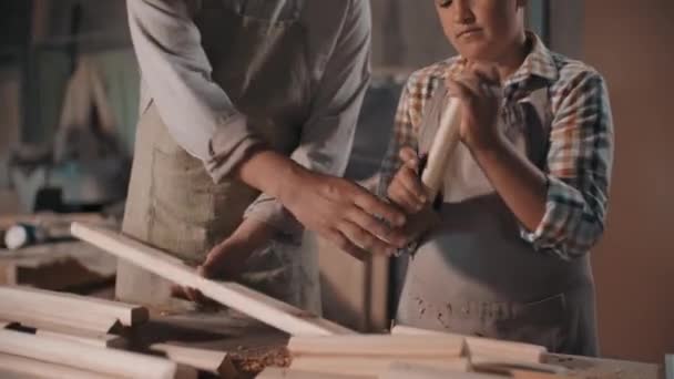 Tilting-up medium footage of little boy sanding wood with sandpaper standing at carpentry table with father helping him making diy furniture - Filmagem, Vídeo