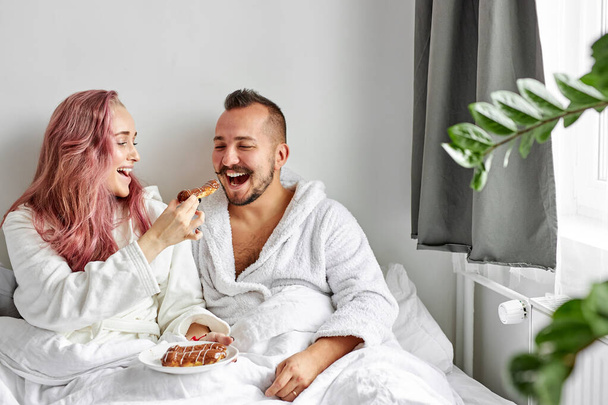 couple treat each other with eclairs on bed - Foto, Imagem