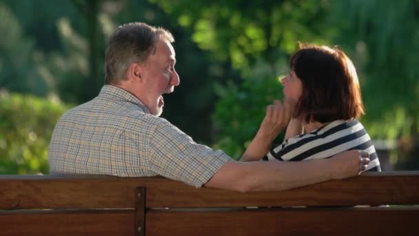 Happy senior couple laughing and joking on bench at park. - Footage, Video