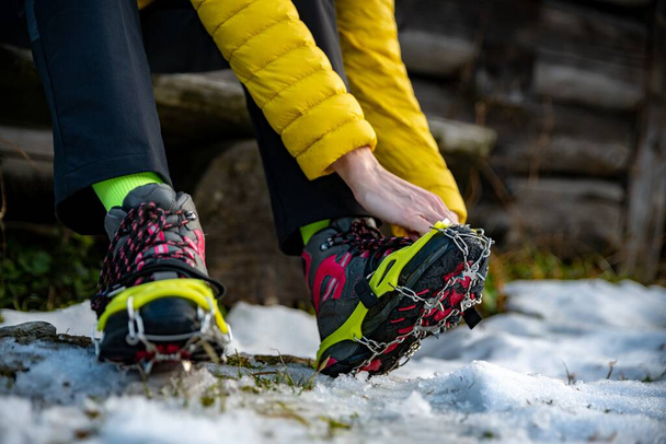 Dłonie kobiet alpinistki noszą raki na buty przed wspinaczką w góry w zimie. - Zdjęcie, obraz