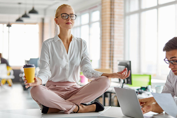 female sits in yoga pose on table at work - Фото, изображение