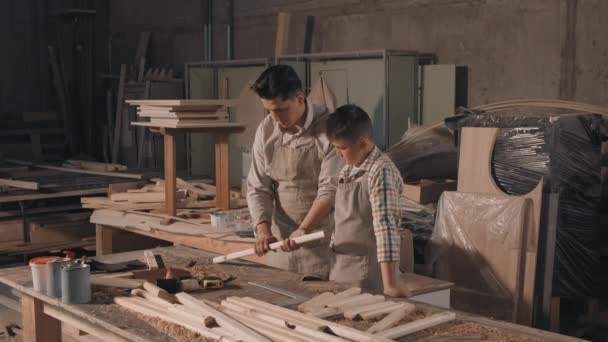 Mediana toma de alegre padre e hijo trabajando en carpintería lijando pieza de madera con lija haciendo muebles de bricolaje juntos - Imágenes, Vídeo