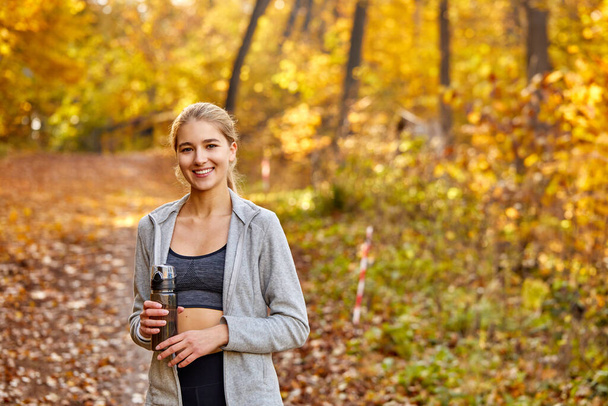 portrait of beautiful blonde female holding bottle of water in the forest - Foto, Imagen