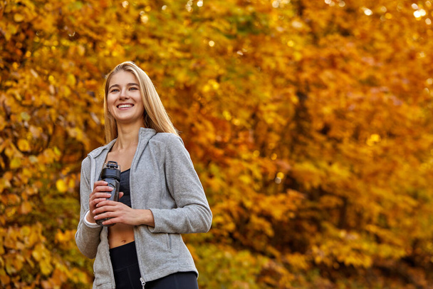 portrait of beautiful blonde female holding bottle of water in the forest - Foto, Imagen