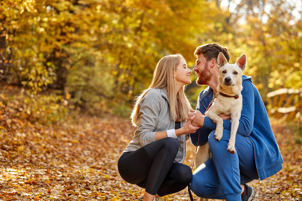 cute caucasian couple dressed casual hugging and taking a walk in nature with their dog - Fotografie, Obrázek