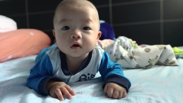Asijský čínský chlapeček leží na posteli a odpykává si břicho. 4k lifestyle záběry rozkošný chlapeček z 5 měsíců dítě - Záběry, video