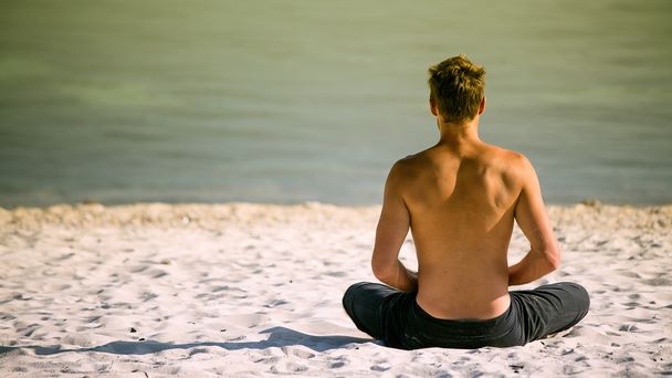 Sitting man doing yoga on shore of ocean - Фото, изображение
