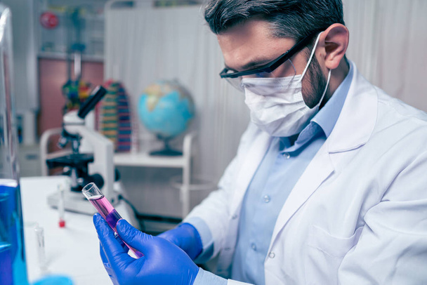 Jovem cientista olhar um tubo de teste no laboratório. Homem usa óculos de proteção - Foto, Imagem