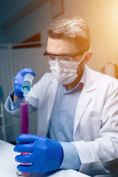 Giovane scienziato che controlla i tubi di prova in laboratorio. Uomo indossa occhiali protettivi - Foto, immagini