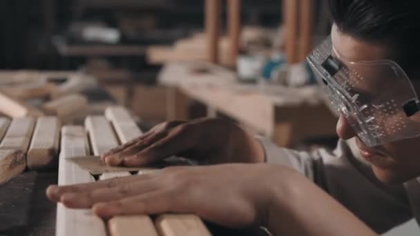 Zbliżenie profesjonalnego rzemieślnika w okularach ochronnych szlifowanie drewnianej powierzchni diy mebli papierem ściernym w warsztacie stolarskim - Materiał filmowy, wideo
