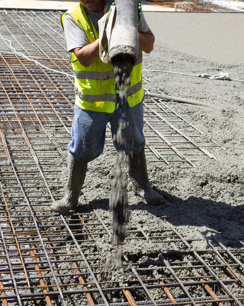 建設中の建物の基礎スラブをセメントが出てくるパイプで埋める労働者 - 写真・画像